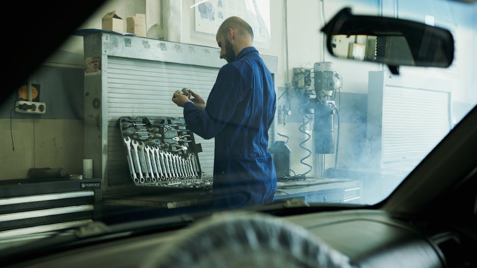 Mechanic in blue overalls working with tools in a smoky garage workshop.